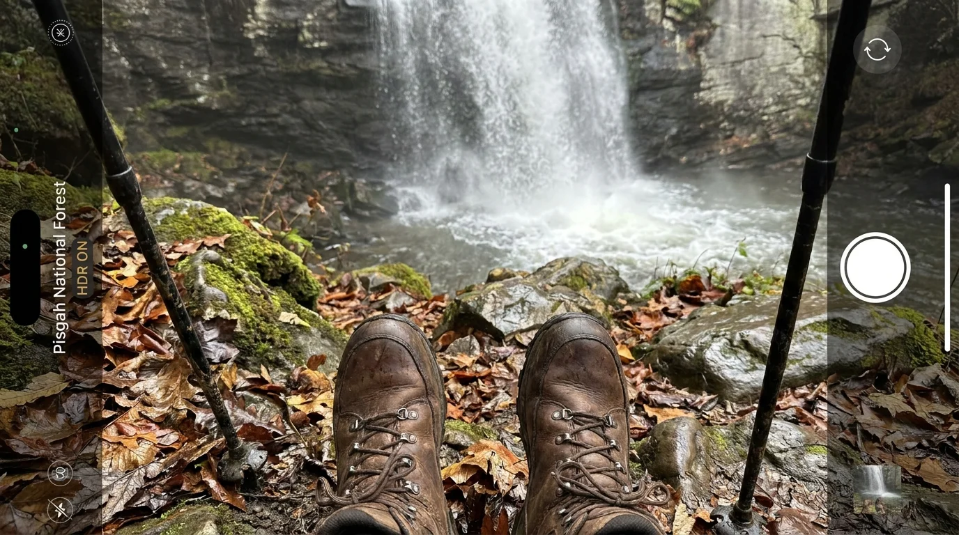 A first-person view of a hiking trail leading toward a misty waterfall in a lush forest.
